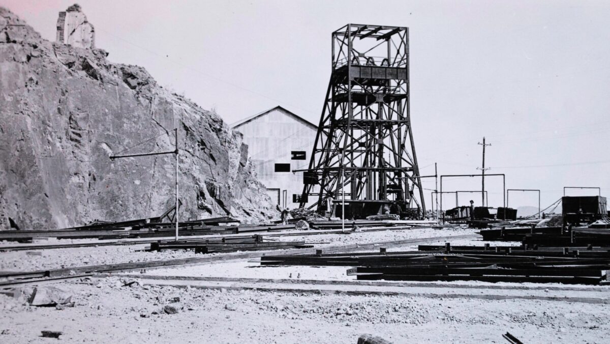 Black-and-white view of the Pilares de Nacozari mining operation in Sonora, Mexico, showing the mine shaft headframe, rail tracks, ore-handling infrastructure, and rugged mountainside landscape during the site's active mining years.