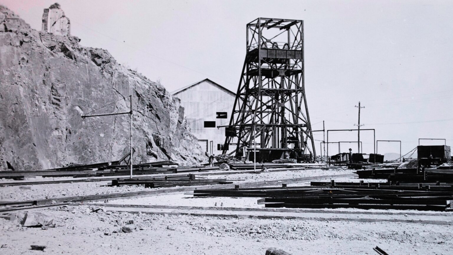Black-and-white view of the Pilares de Nacozari mining operation in Sonora, Mexico, showing the mine shaft headframe, rail tracks, ore-handling infrastructure, and rugged mountainside landscape during the site's active mining years.